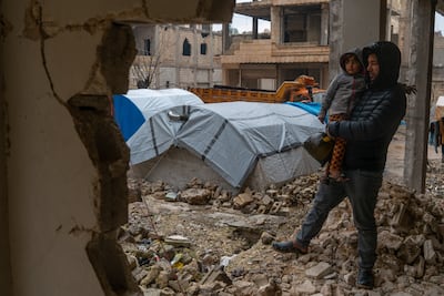 Syrian Ahmed Masto, 30, carries his son among the ruins of their house, which was destroyed by last year's earthquake. Next to them is the tent in which they now live. Moawia Atrash / The National