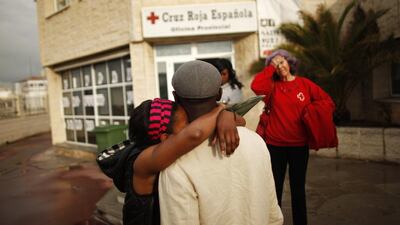 A member of Spanish Red Cross looks at two immigrants embracing after they learnt that they will be moved to different reception centres in separate Spanish cities, upon their arrival from Melilla at Malaga port, southern Spain. Jon Nazca / Reuters
