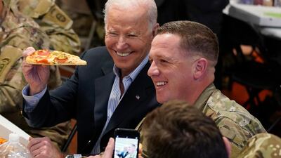 Mr Biden holds a slice of pizza during his meeting with US troops. AP