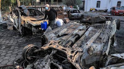 A man carries salvaged items past destroyed vehicles at the site of Al Ahli Arab Hospital in central Gaza on Wednesday. The devastation at the hospital is shaping up to be the bloodiest single incident of the current conflict so far. AFP