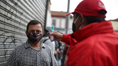 A man takes a customer's body temperature wearing a face mask before entering a shopping area, after the Colombian government decided to relax social restrictions amid the outbreak of the coronavirus disease, in Bogota, Colombia. Reuters