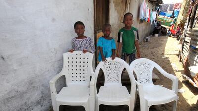 Brothers Fatu Hawa, left, Frances, centre and Raymond Risks pose for a family portrait at their home in West Point, Monrovia, Liberia. The empty chairs symbolise of their father, mother and brother who died of the Ebola virus during an outbreak of the disease in 2014. Ahmed Jallanzo / EPA