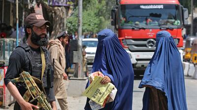 Burqa-clad women walk past a Taliban security agent along a street in Jalalabad. AFP