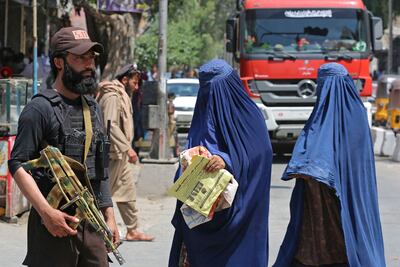 Afghan women wearing chadari garments walk past a Taliban security officer in Jalalabad in April. AFP