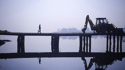 A labourer walks near a parked bulldozer at the construction site of a bridge being built over the Yamuna river for the metro rail in New Delhi. Anindito Mukherjee / Reuters