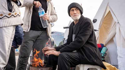 A man warms his hands by a fire at a camp in Osmaniyeh