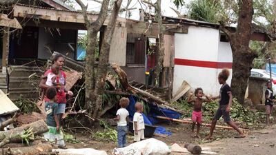 A woman carrying a baby stands with children outside homes damaged by Cyclone Pam, on a street surrounded by debris in Port Vila, the capital city of the Pacific island nation of Vanuatu March 15, 2015. Kris Paras/Reuters