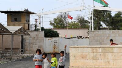 This picture taken from the Syrian Kurdish town of Kobane, along the border with Turkey in the north of Aleppo governorate, shows children standing by (foreground) a Syrian Kurdish Yellow-Red-Green Rojava flag and (background) a Turkish national flag flying across both sides of the border between Syria and Turkey. AFP