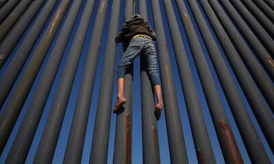 A migrant, part of a caravan of thousands from Central America trying to reach the United States, climbs the border fence between Mexico and the United States, in Tijuana. Reuters