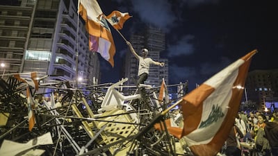 An anti-government protester waves a Lebanese flag as he stands on top of a pile of broken tents in Martyrs' Square in Beirut, Lebanon. Getty Images