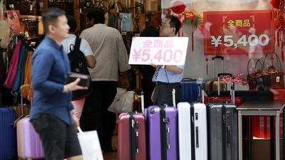 A shop clerk holds a price banner at a bag shop in Tokyo. Underlying weakness means the Bank of Japan will probably expand its asset purchases further, analysts said. Eugene Hoshiko/AP