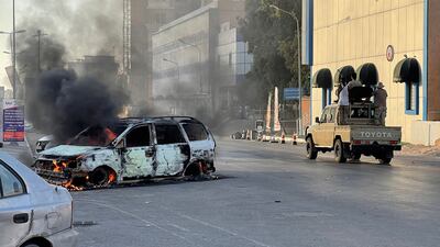 Fighters loyal to Libya's Government of National Unity pass a burning car on a street in Tripoli following clashes between militias. AFP