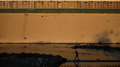 A man is reflected as he makes his way on the Tijuana river as the pedestrian bridge border crossing between the US and Mexico is seen in the background, in Tijuana, Mexico. Reuters