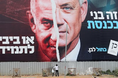 A boy looks up at a Blue and White coalition campaign hoarding depicting its leader, Benny Gantz, alongside Israeli Prime Minister Benjamin Netanyahu, for the March 2021 election. Reuters