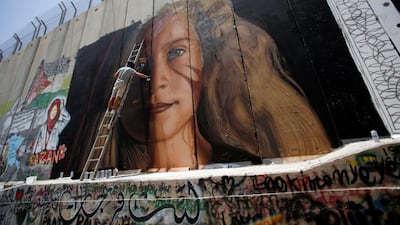 A foreign artist paints on the Israeli wall a mural depicting Palestinian teen Ahed Tamimi who is detained by Israel, in Bethlehem, in the occupied West Bank. REUTERS/Mussa Qawasma