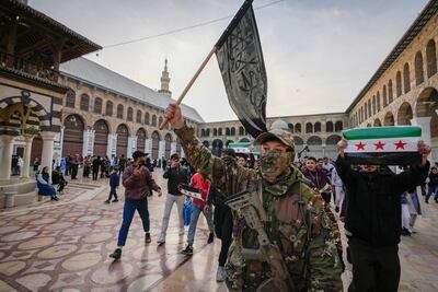 A masked opposition fighter carries a flag of Hayat Tahrir Al Sham (HTS) in the courtyard of the Umayyad Mosque in Damascus, Syria, on Tuesday, December 10, 2024. AP