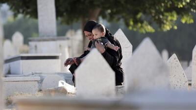 A Palestinian woman holds a child as she pays her respects at a relative's grave in a cemetery in Gaza City on Saturday. Khalil Hamra / AP Photo