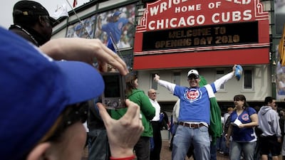In this April 12, 2013 file photo, Ben Martin, from St Louis, has his picture taken by friend Stephanie Martin before a baseball game and Cubs home opener against the Milwaukee Brewers at Wrigley Field in Chicago. The famed marquee, scoreboard and ivy were not original parts of the ballpark. The marquee went up in 1934 and was more of a bluish color at the time. The ivy was installed three years later. The scoreboard originally was a reddish brown with a white clock and was painted its familiar dark green in 1944. Charles Rex Arbogast / AP