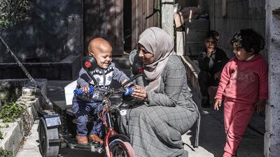 The mother of Zain, a five-year-old Palestinian boy with disability, holds his hand as he sits atop an electric vehicle assembled by Abu Raida in Bani Suhaila, a town east of Khan Yunis in the south of the Gaza Strip. AFP