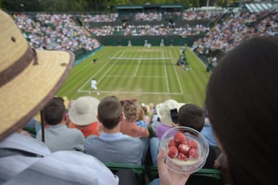 A spectator eats strawberries and cream as she watches play at Wimbledon. The tennis tournament boost sales of strawberries and cream in UK supermarkets Carl Court / AFP