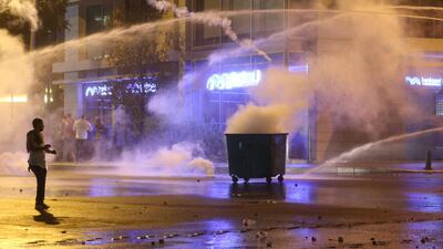 Lebanese protesters take shelter as tear gas canisters and water cannons are used to disperse them during clashes with security forces. AFP / STR