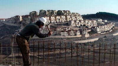 A man works on a construction site in Bethlehem, Palestine, as illegal settlements tower in the distance (AFP / AHMAD GHARABLI)