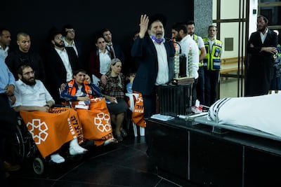 Avigdor Hayut, who was hurt in the deadly stampede at Mount Meron, sits on a wheel chair near his son, Shmuel Hayut, who was also hurt at the stampede and his wife as his father is speaking at the funeral of his son Yedidia Hayut, 13. Getty Images