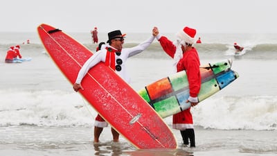 George Trosset Jr. and George Trosset, who started surfing in Christmas costumes ten years ago, high five each other during the 10th annual Surfing Santas event in Cocoa Beach, Flordia. AP
