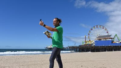 This picture taken on March 23, 2020 shows Adam Duford, owner of Surf City Tours, describing iconic sites in Santa Monica, California as part of a "virtual tour" via his Instagram feed, as the COVID-19 novel coronavirus situation forced his normal tour bus business to come to a halt. / AFP / Robyn Beck
