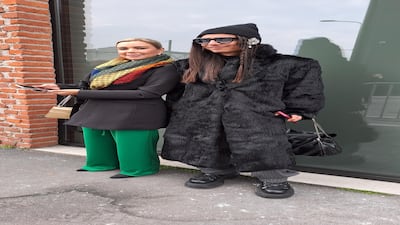 In a vintage fur coat and a beanie hat, this man looks very stylish, while his friend matches a patterned scarf with green trousers