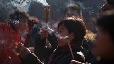 A woman burns incense at the Lama Temple in Beijing. Mark Schiefelbein / AP Photo