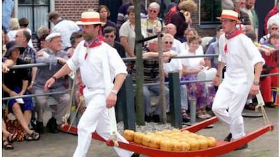 Tourists watch two traditionally dressed man carry a tray of cheese in Edam.