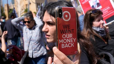 A bank customer holds up her mobile phone bearing a sticker saying "we want our money back" during a protest in Beirut, Lebanon. AP