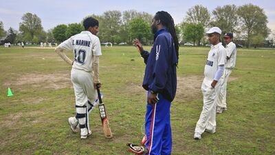 In this May 12, 2014 photo, Linden Fraser, second from left, New York regional cricket head coach, chats with John Adams High School player Derick Narine, left, before he bats in a match against Midwood High School . Fraser, also a coach for the US women's national cricket team, often makes the rounds to high school matches to offer advice and support. Bebeto Matthews / AP
