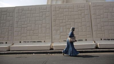 A Palestinian woman walks past a temporary concrete wall bearing black lettering reading in Hebrew "temporary mobile police barrier" that was erected by Israeli police, in the East Jerusalem neighbourhood of Jabal Mukaber. Ahmad Gharabli / AFP
