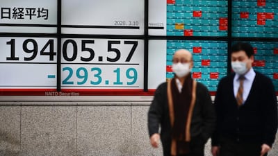 Mask-clad pedestrians walk past a quotation board displaying the share price index of the Tokyo Stock Exchange in Tokyo. AFP
