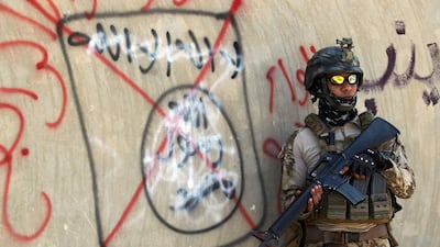 An Iraqi soldier stands next to a wall with a red cross above a slogan of the Islamic State (IS) group, in the city of Fallujah. Ahmad Al Rubaye / AFP