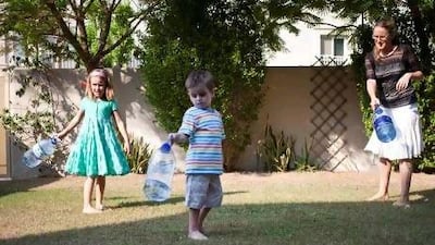 Tabitha Rayer, 6, Tasker Rayer, 3, and their mother Alice Haine water the grass in the garden of their home with bottled water during their experiment using just bottled water for a weekend. Razan Alzayani / The National