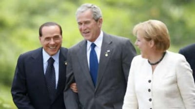 The Italian prime minister Silvio Berlusconi holds on to the arm of President George Bush as the German chancellor Angela Merkel looks on before posing for the official photo at the G8 summit today.