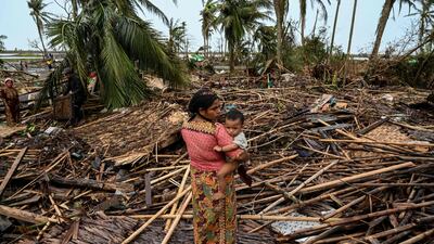 A Rohingya woman carries her baby next to her destroyed house at Basara refugee camp, in Sittwe. AFP