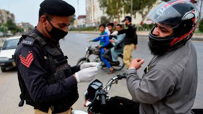A policeman checks the ID card of a motorcyclist Karachi during a lockdown across Pakistan's Sindh province that began on March 23, 2020. AFP