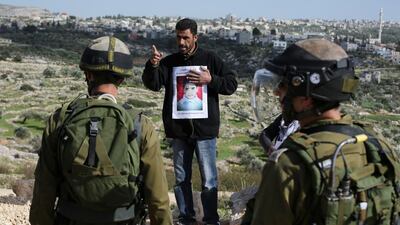A protester from the West Bank village of Bilin holds a portrait of Malak Al Khatib, 14, who was arrested for throwing stones, as he confronts Israeli soldiers during a march against Israeli settlements on January 30, 2015. Abbas Momani / AFP