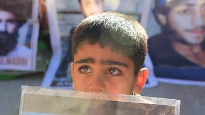 a little kid with tearful eyes is holding the picture of his missing father during the demonstration. Rabia Bugti for The National