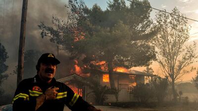 A firefighter reacts as a house burns during a wildfire in Kineta, near Athens. AFP