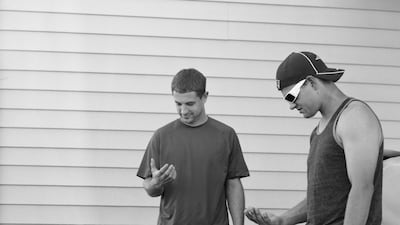 Two men stare off into their hands while waiting by a barbecue grill. Courtesy Eric Pickersgill