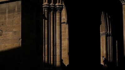 A woman, right, walks as a man, left, is silhouetted as he sits on a bench outside of the Selimiye mosque in Nicosia, Cyprus, Monday, Dec. 3, 2018. AP