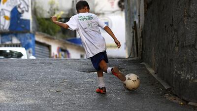 A young favela boy kicks his football on a street in Rocinha. Barbara Walton / EPA