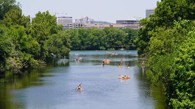 Kayakers and paddle boarders float along the Colorado River with the Austin skyline in the background.