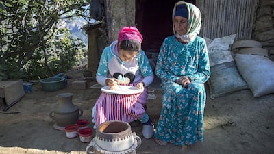 Houda Oumal paints with natural pigments on one of her pieces of pottery as her mother Fatima Harama looks on. AFP