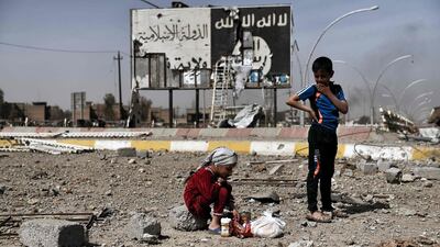 Iraqi children sit amidst the rubble of a street in Mosul's Nablus neighbourhood in front of a billboard bearing the ISIL logo. Aris Messinis / AFP